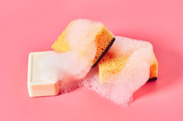 Brick of soap with foam bubbles near sponge on pink background. Washing, cleaning concept