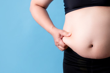 Overweight woman catches fat on her belly on a blue background. Isolated background