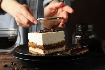 Girl sprinkles powder on tiramisu. Composition with tasty cake on wooden background