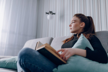 Naklejka premium young attractive girl on the couch reads a paper book. mental development. useful use of time at home. home comfort.
