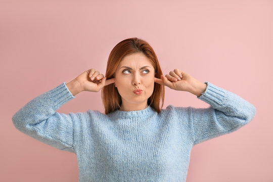 Young woman suffering from loud noise on color background