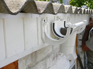 Obraz premium A close up on a plastic running outlet and fascia brackets fixed to the fascia board during rain gutter system roof installation.