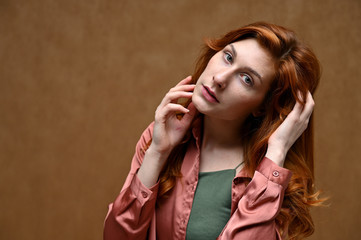 Obraz premium Studio shot with even emotions. Photo portrait on a beige background of a caucasian calm pretty young woman in a pink shirt with long beautiful red hair.