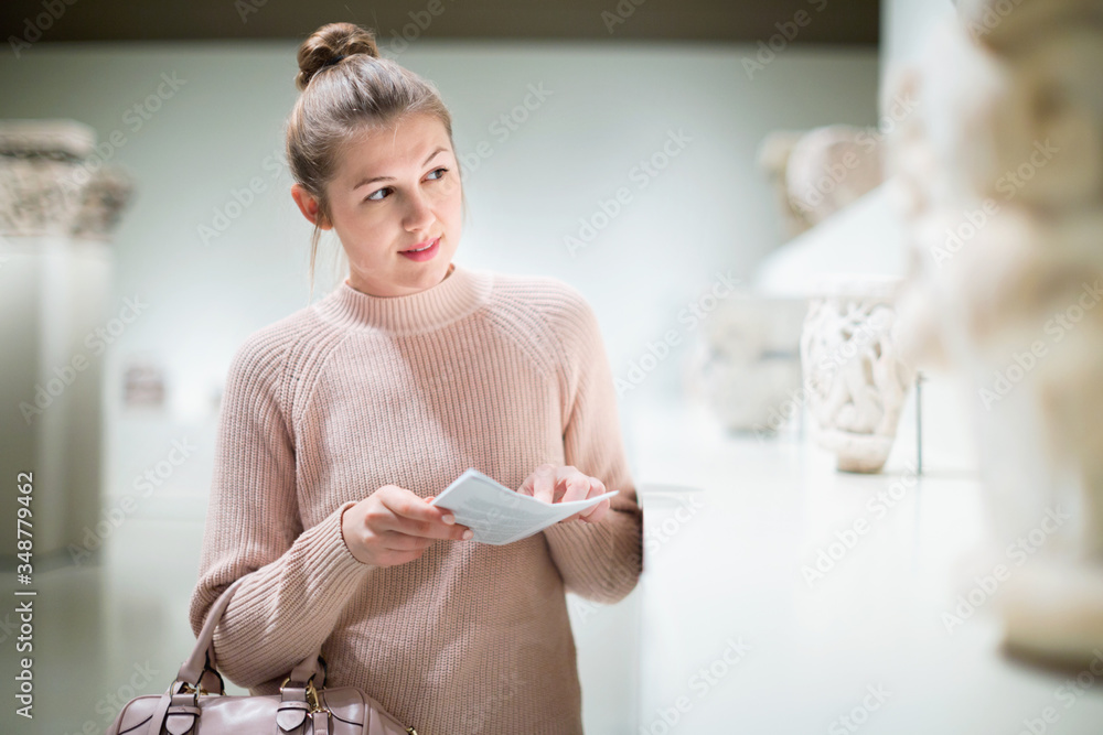 Wall mural girl looking with interest at ancient sculptures in museum, using guidebook