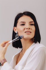 Attractive young business girl with makeup brushes posing on plain background. concept of makeup and cosmetics.