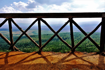 Great Rift Valley in Kenya. The railing of the observation deck is wooden, the floor is made of red clay. The endless plain is covered with jungle, the silhouettes of mountains. Beautiful clouds.