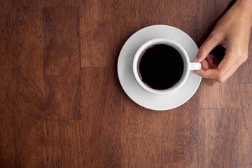 Top view of hand is holding black coffee cup on wooden background.