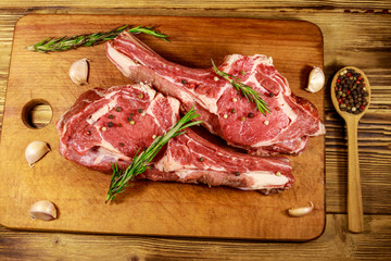Raw fresh beef rib eye steak on bone with spices, garlic and rosemary on wooden table. Top view