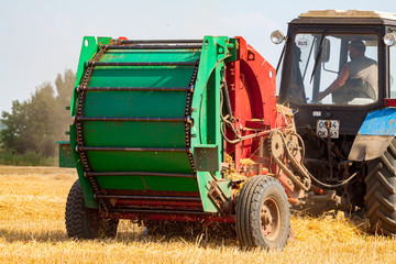 A tractor with a trailed bale making machine collects straw rolls in the field and makes round...