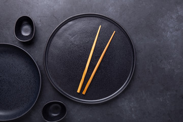 Set of dark plates and chopsticks on stone background. Set for Asian, Japanese and Chinese food
