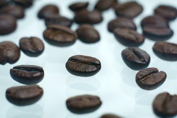 Roasted coffee beans pile on white glass reflection background
