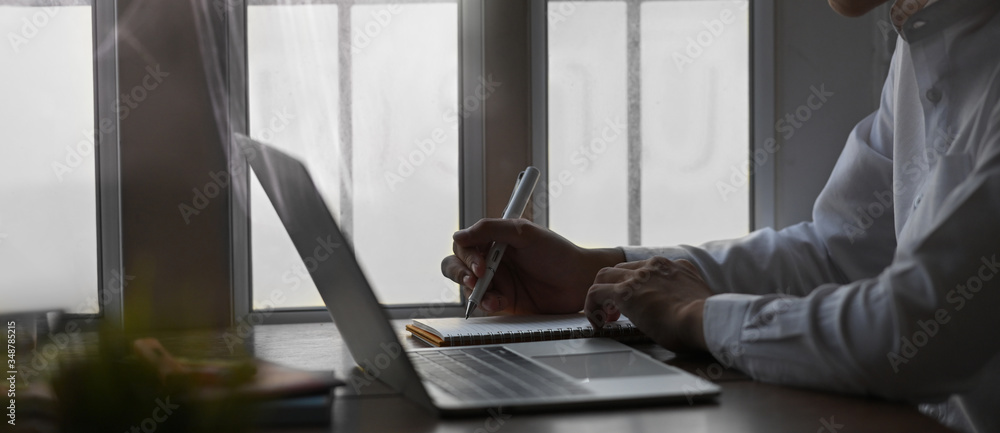 Poster cropped image of businessman taking notes while sitting in front of computer laptop that putting on 