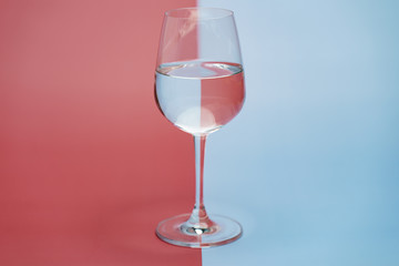 Transparent glass of water, clean drinking water in a clear glass  on two tone (pink and blue) background