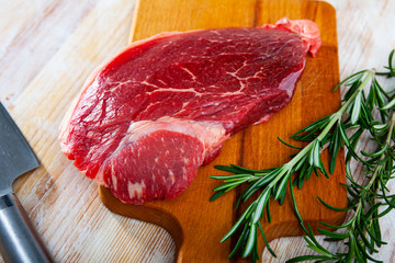 Unfinished beef steak with sprig of rosemary on cutting board