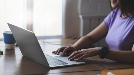 Woman smiling and typing on computer laptop that putting on wooden working desk over modern sitting room brick wall as background.