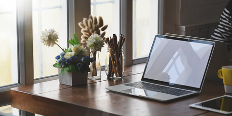 Computer laptop putting together on wooden working desk with potted of flowers, pencils in glass vase, computer tablet and coffee cup.