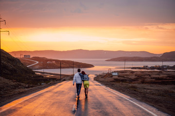Young couple on the way to the Barents Sea on a wet road in a sunset