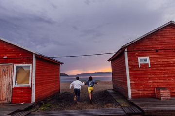Young couple running on the way to the Barents Sea on a wet sand in a sunset of polar day