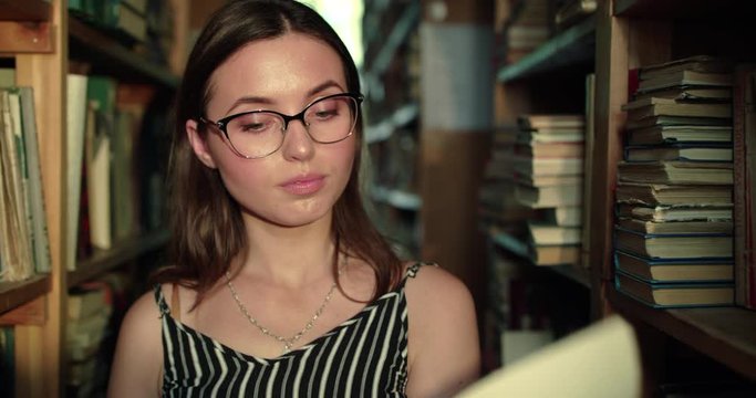 Girl flips through the book and looks about it with joy among shelves in library