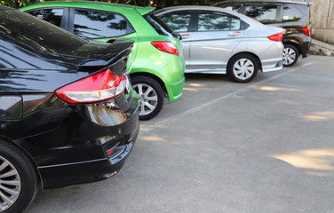 Closeup of rear, back side of black car with other cars parking in outdoor parking area.
