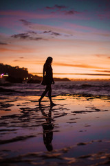 Young woman silhouette on a seashore in sunset with colourful skies and wet reef