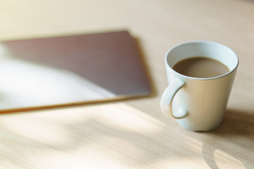 Work desk with a laptop computer, a cup of coffee, with morning sunlight.