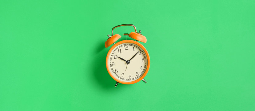 Orange vintage alarm clock on green background. Top view. Flat lay