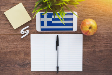 Greece flag, smartphone, wireless headphones, a notebook for writing foreign words on a working wooden table, the concept of learning a foreign language  © Evgeniia Primavera