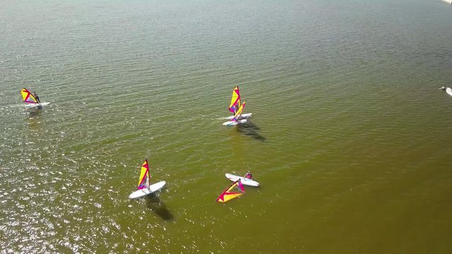 Aerial following profile shot of beginner windsurfer. Other summer camp participants are losing balance while our hero remains strong.