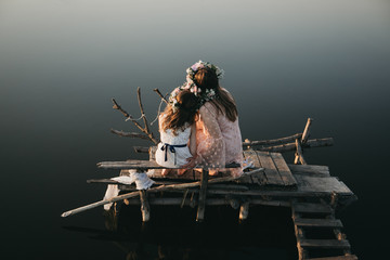 Mom and daughter are sitting on a wooden bench, a wooden bridge and looking at a beautiful river....