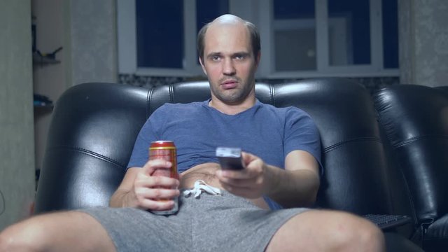 lonely balding man at home in a chair with a beer and a remote control.