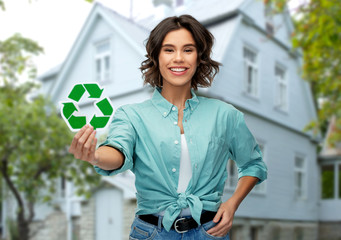 eco living, environment and sustainability concept - portrait of happy smiling young woman in turquoise shirt holding green recycling sign over house on background