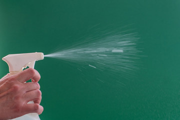 Closeup female hand spraying antibacterial disinfectant to clean home and office on green background. Sanitizer for the prevention of Coronavirus or Covid-19, influenza. Spray. Copy space