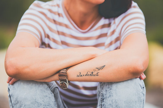 Mujer sentada con tatuaje Wanderlust en el antebrazo