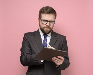 Serious man in a suit writes with a stylus on a tablet and looks suspiciously, thoughtfully at the...