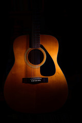 Acoustic guitar on a black background between light or shadows