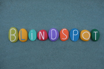 Blindspot word composed with multi colored stone letters over green sand