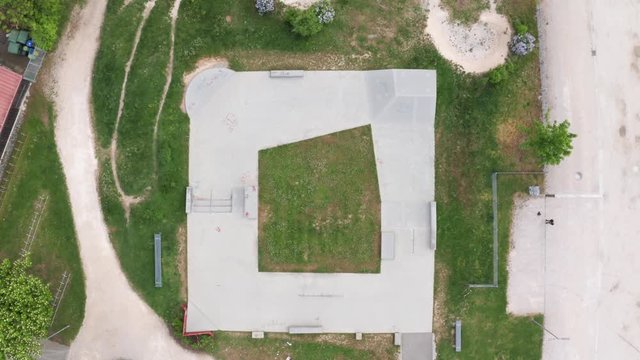 Looking at an empty skatepark from above. Drone drops slowly, from super wide to medium wide. Very geometrical layout of the park. Aerial shot of a skatepark, looking down.