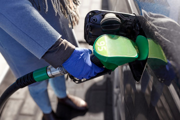 health, safety and pandemic concept - close up of hand in glove filling car with gasoline at gas station