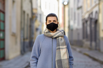 health, safety and pandemic concept - young woman wearing black face protective reusable barrier mask on empty city street