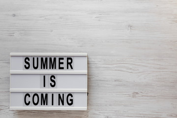 'Summer is coming' text on a modern board on a white wooden background, top view. Flat lay, overhead, from above. Copy space.