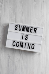 Obraz premium 'Summer is coming' text on a lightbox on a white wooden background, top view. Flat lay, overhead, from above.