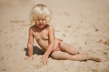 Little girl is playing in the sand. Girl sitting on a sandy beach. Summer mood. Rest by the sea.