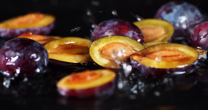 The slices of fresh plums falling water drops with splash.