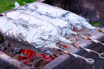 Juicy and fresh slices of pork are strung on metal skewers, wrapped in aluminum foil and grilled on...