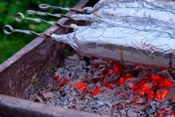 Juicy and fresh slices of pork are strung on metal skewers, wrapped in aluminum foil and grilled on...
