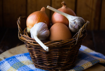 Chicken eggs. Brown chicken eggs in basket on the cutting board on wooden background, close up. Still life with eggs, garlic, onion. Farm natural products. Egg and vegetables is ingredient for cooking