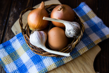 Chicken eggs. Brown chicken eggs in basket on the cutting board on wooden background, close up. Still life with eggs, garlic, onion. Farm natural products. Egg and vegetables is ingredient for cooking
