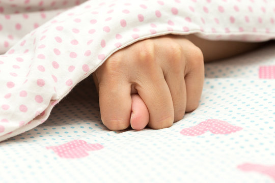Beautiful female hand shows a fig sign under a white blanket, hands showing thumb. Offensive sign Dulia.