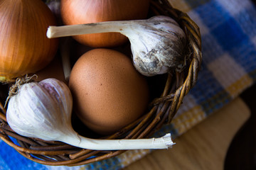 Chicken eggs. Brown chicken eggs in basket on the cutting board on wooden background, close up. Still life with eggs, garlic, onion. Farm natural products. Egg and vegetables is ingredient for cooking
